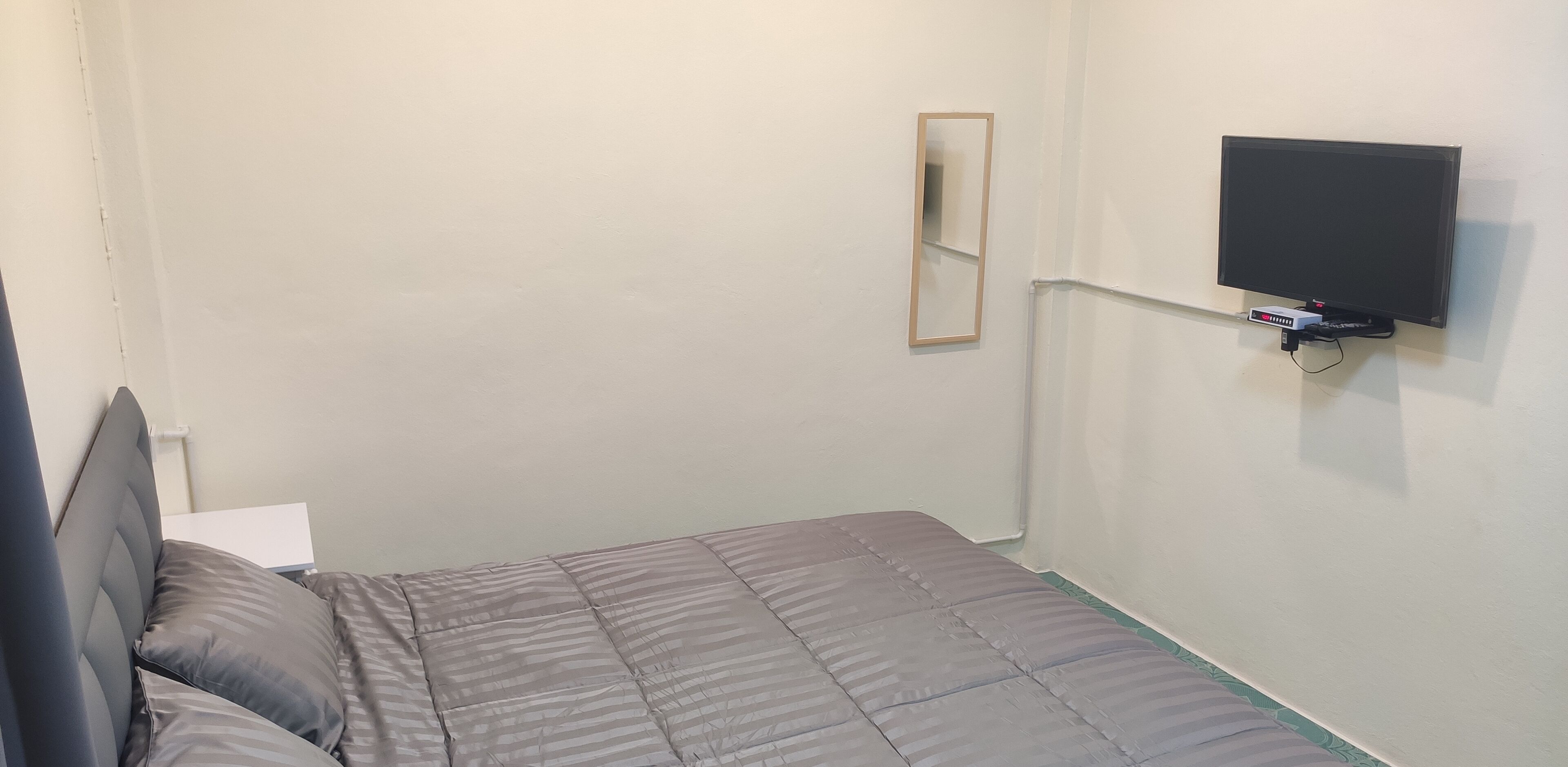 A bedroom with a bed, a TV mounted on the wall, and a mirror.
