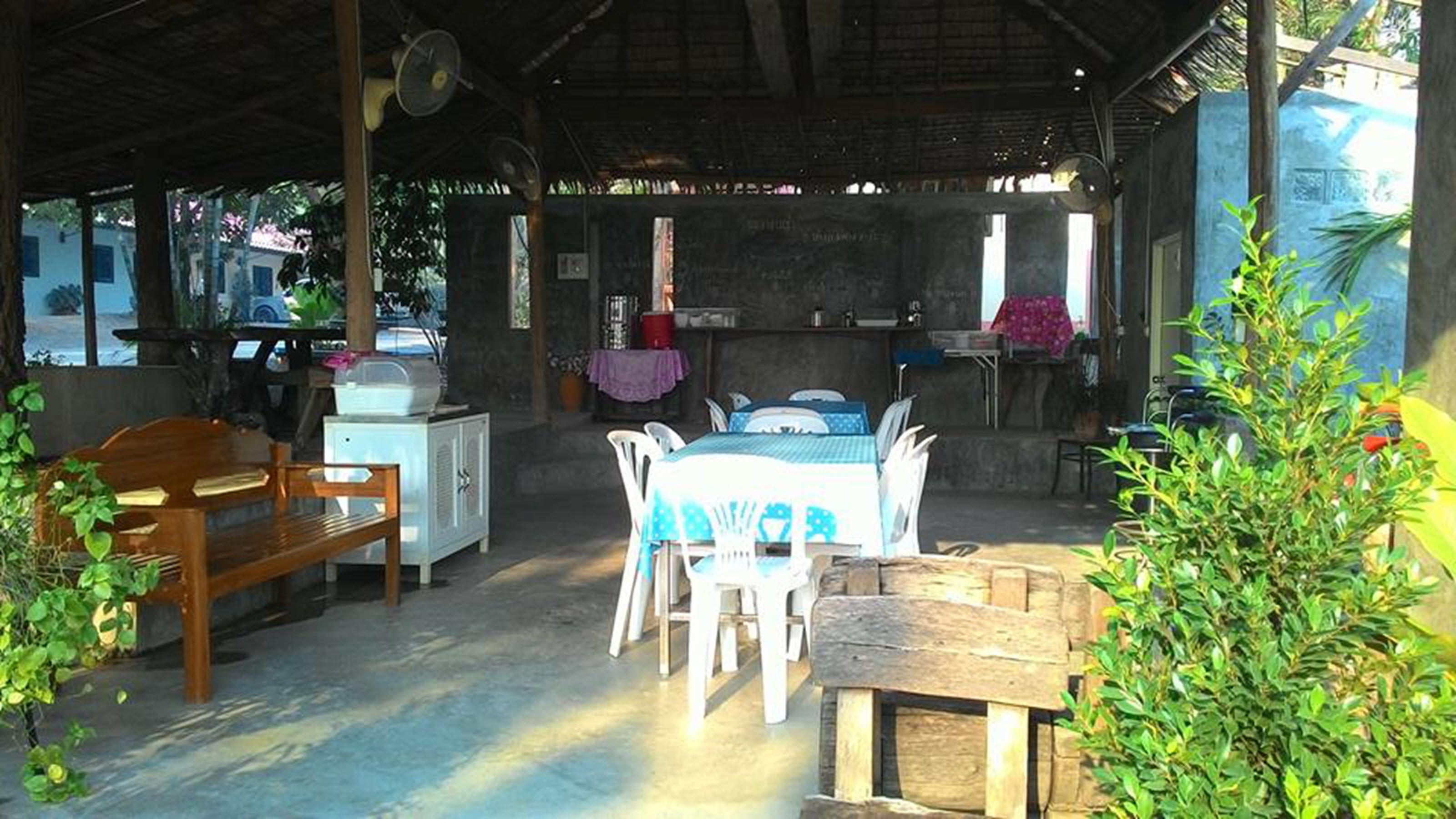 An outdoor dining area with a table and chairs, a refrigerator, and a wooden bench.