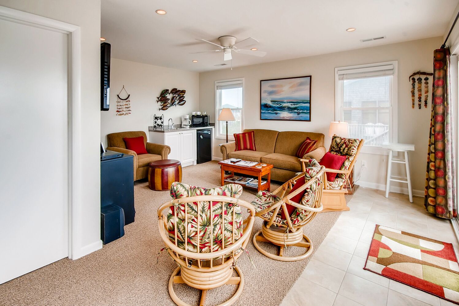 A spacious living room with a sofa, two wicker chairs, a coffee table, and a kitchen area in the background.