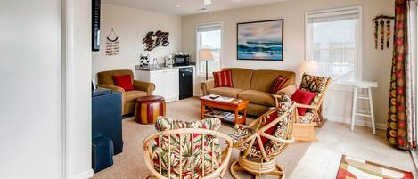 A spacious living room with a sofa, two wicker chairs, a coffee table, and a kitchen area in the background.