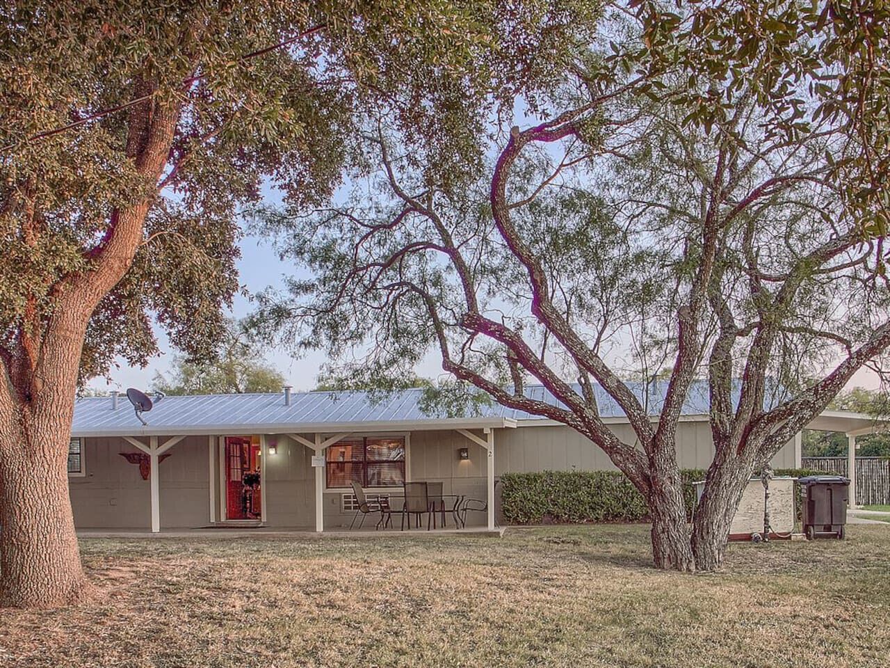 A single-story building with a covered porch, a satellite dish, and a red door.