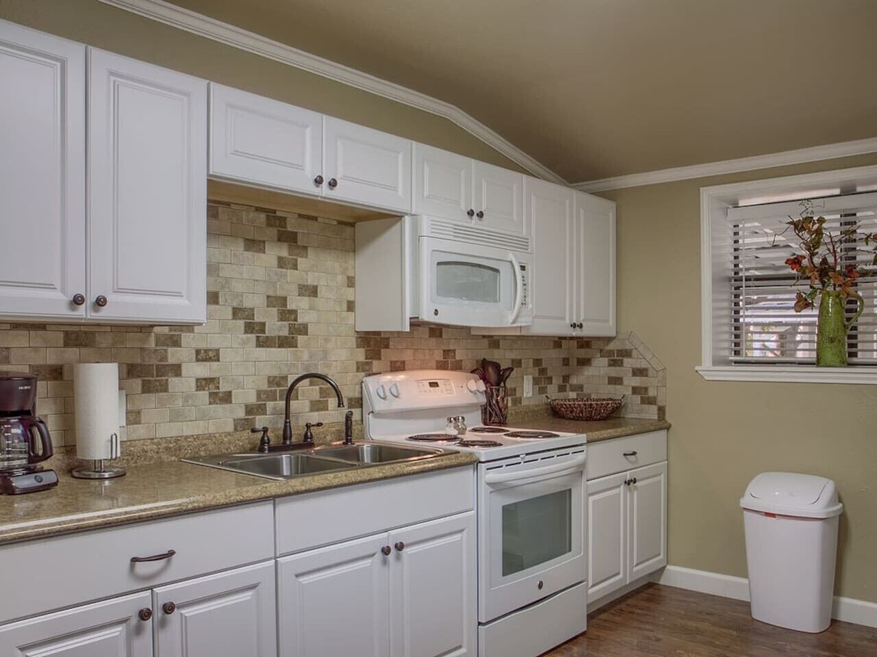 A kitchen with white cabinets, a microwave, stove, and a sink.