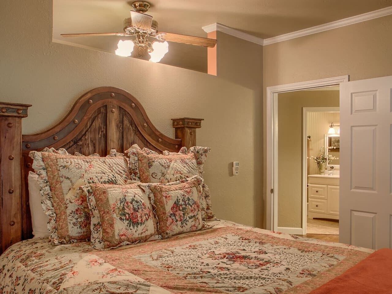A bedroom with a wooden headboard, floral bedding, and a ceiling fan.
