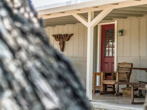 Un portico con sedie di legno e una porta rossa, un cartello di legno con la scritta "TEXAS" e un fioralino di luce fissato al muro.