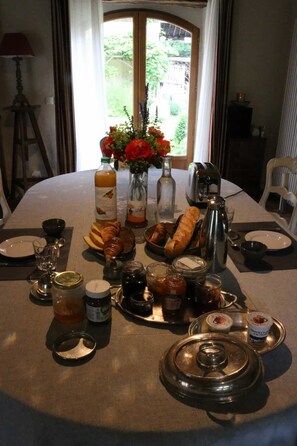 A dining table set with various food items, condiments, and glassware, with a window view in the background. - Le Bourgis chambres d'hotes (La Chapelle-Montligeon)