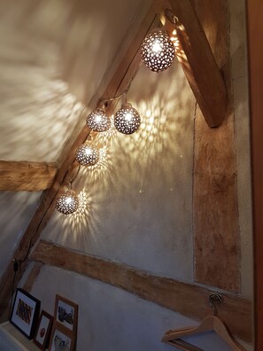 A sloped ceiling with wooden beams and a series of spherical, perforated light fixtures casting patterns on the wall. - Le Bourgis chambres d'hotes (La Chapelle-Montligeon)