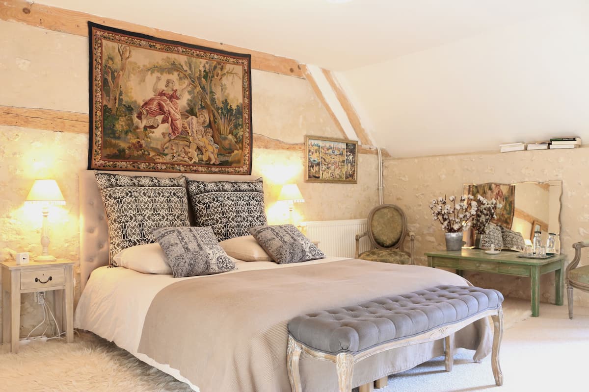 A bedroom with a large bed, a bench, a nightstand, a dresser, and a painting on the wall.
