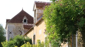 A historic building with a red-tiled roof, surrounded by lush greenery and flowering plants. - Le Bourgis chambres d'hotes (La Chapelle-Montligeon)