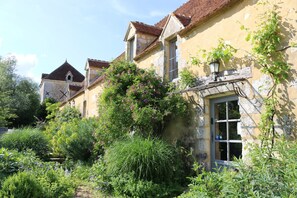 Un bâtiment historique doté d’une façade en pierre, d’un toit à pignon traditionnel et d’une petite fenêtre avec un volet en bois.