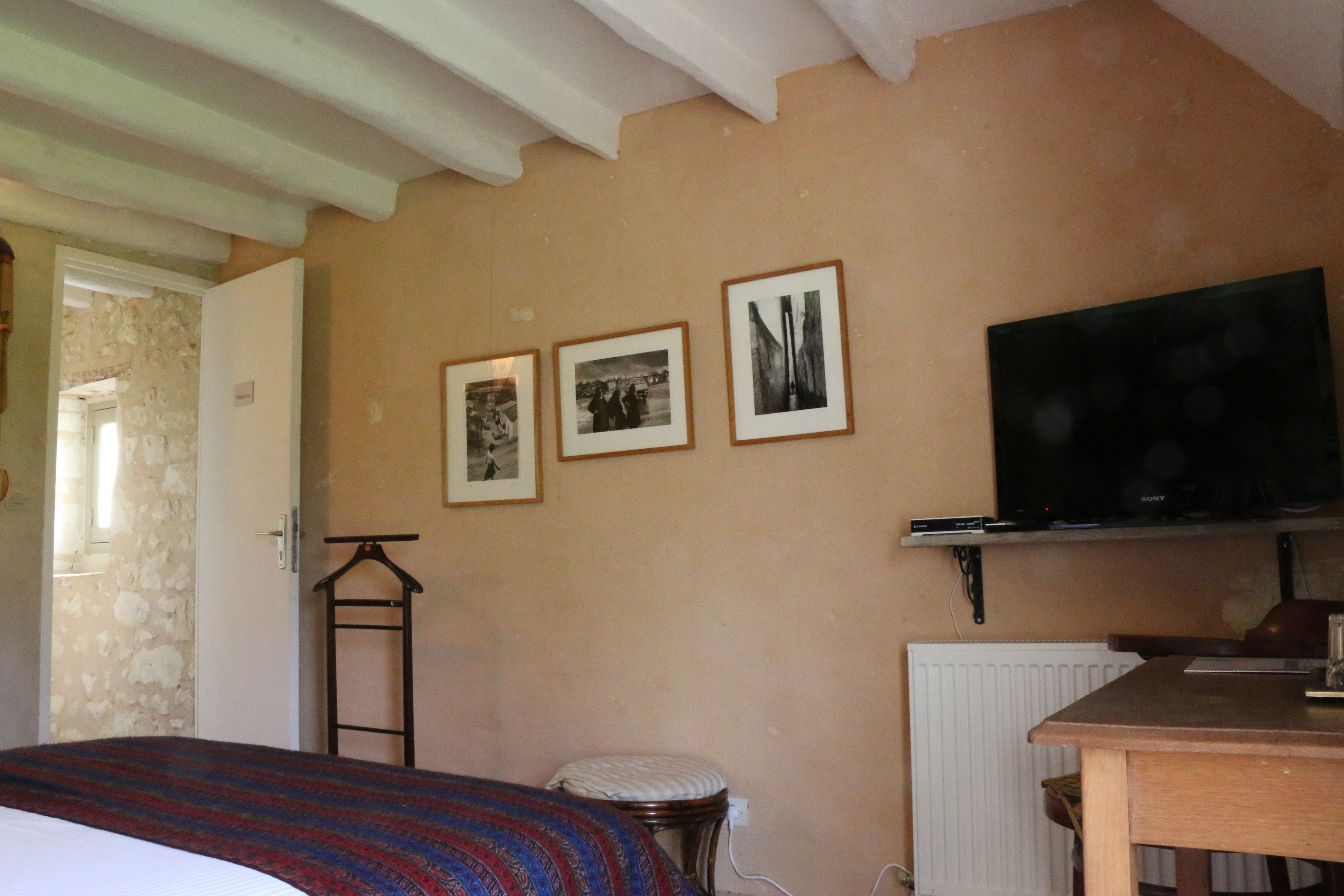 Een slaapkamer met een bed, een televisie en drie ingekaderde foto’s aan de muur.