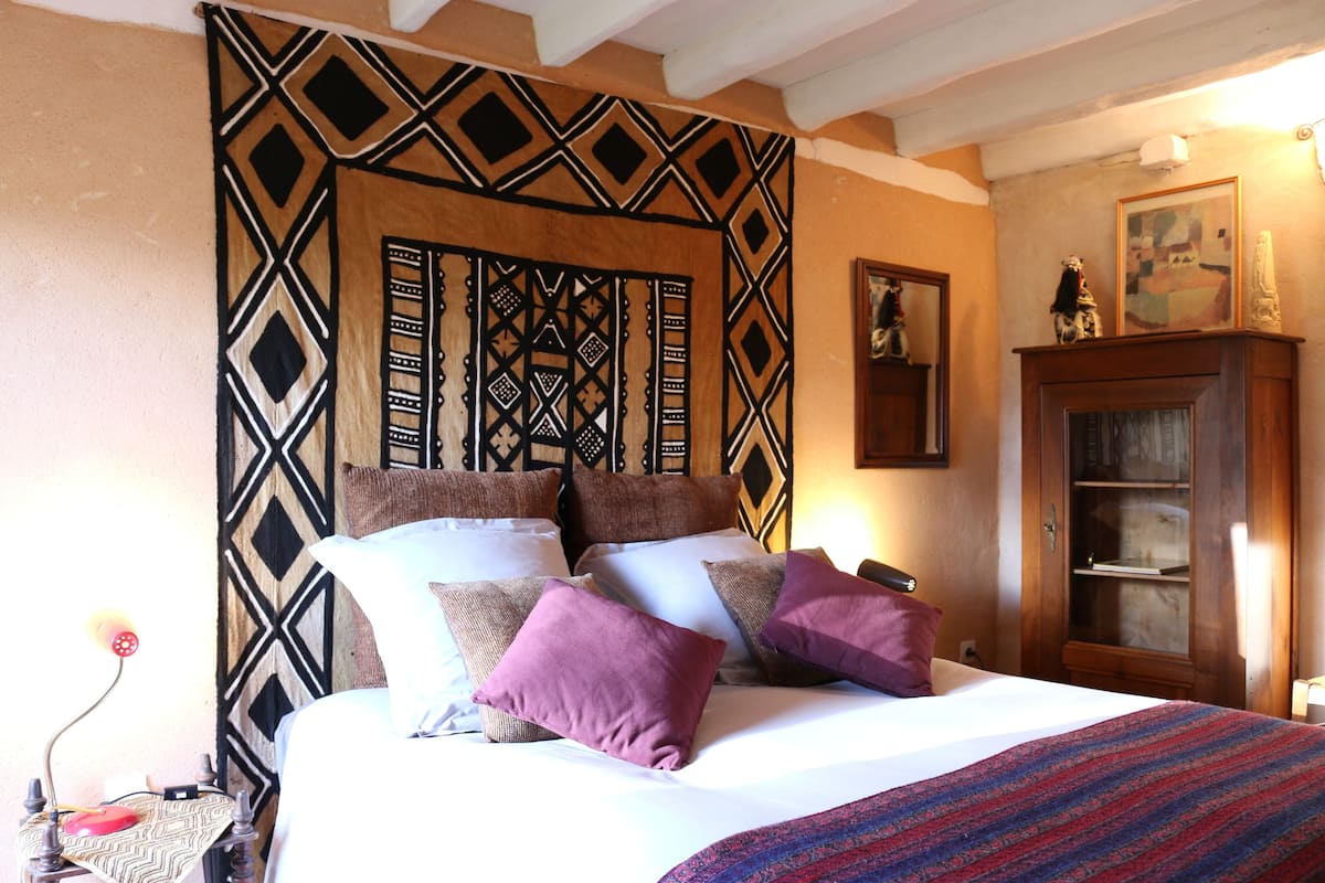 A bed with multiple pillows, a patterned headboard, a wooden cabinet, and a framed picture on the wall.