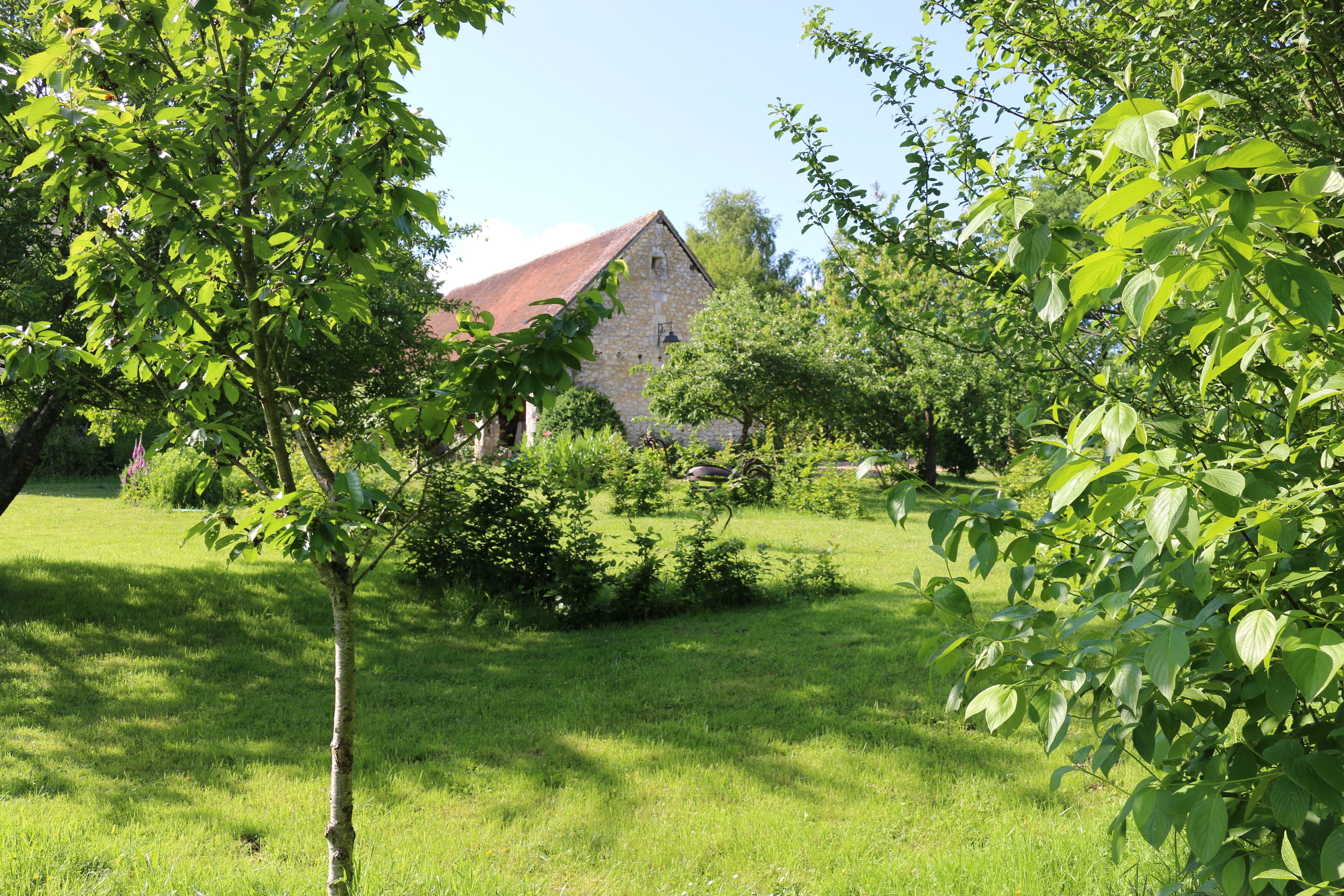 A stone building with a red roof surrounded by lush green grass and trees.