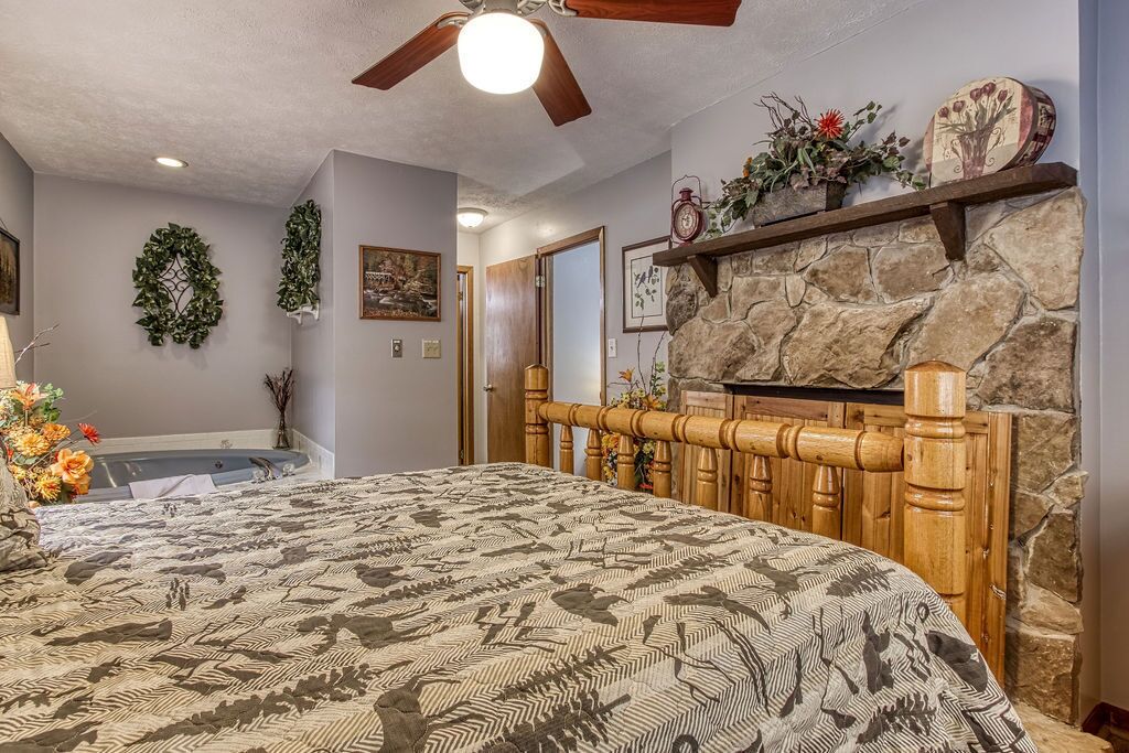 Ein Schlafzimmer mit einem großen Bett, einem Kamin aus Stein, einem Deckenventilator und einem an der Wand befestigten Regal mit Dekorationen.