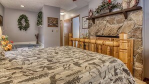 Un dormitorio con una cama grande, una chimenea de piedra, un ventilador de techo y un estante empotrado con objetos decorativos.