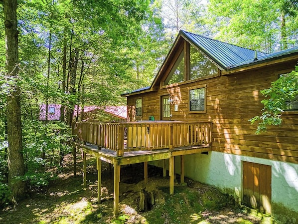 Una cabaña de madera con terraza, rodeada de un bosque denso.