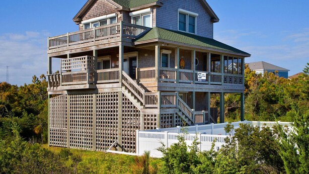A two-story house with a balcony and a deck, surrounded by greenery. - Oceanview Home w/ Private Pool, Hot Tub, and Game Room. It's Simply Irresistible (Waves)