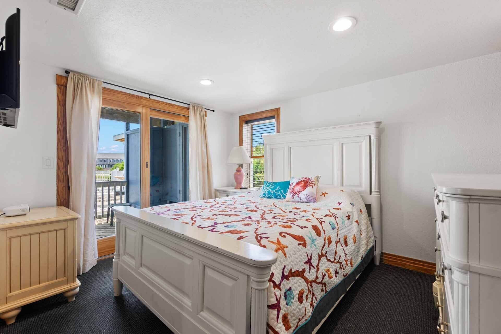 A bedroom with a bed, a dresser, a nightstand, and a window with curtains.