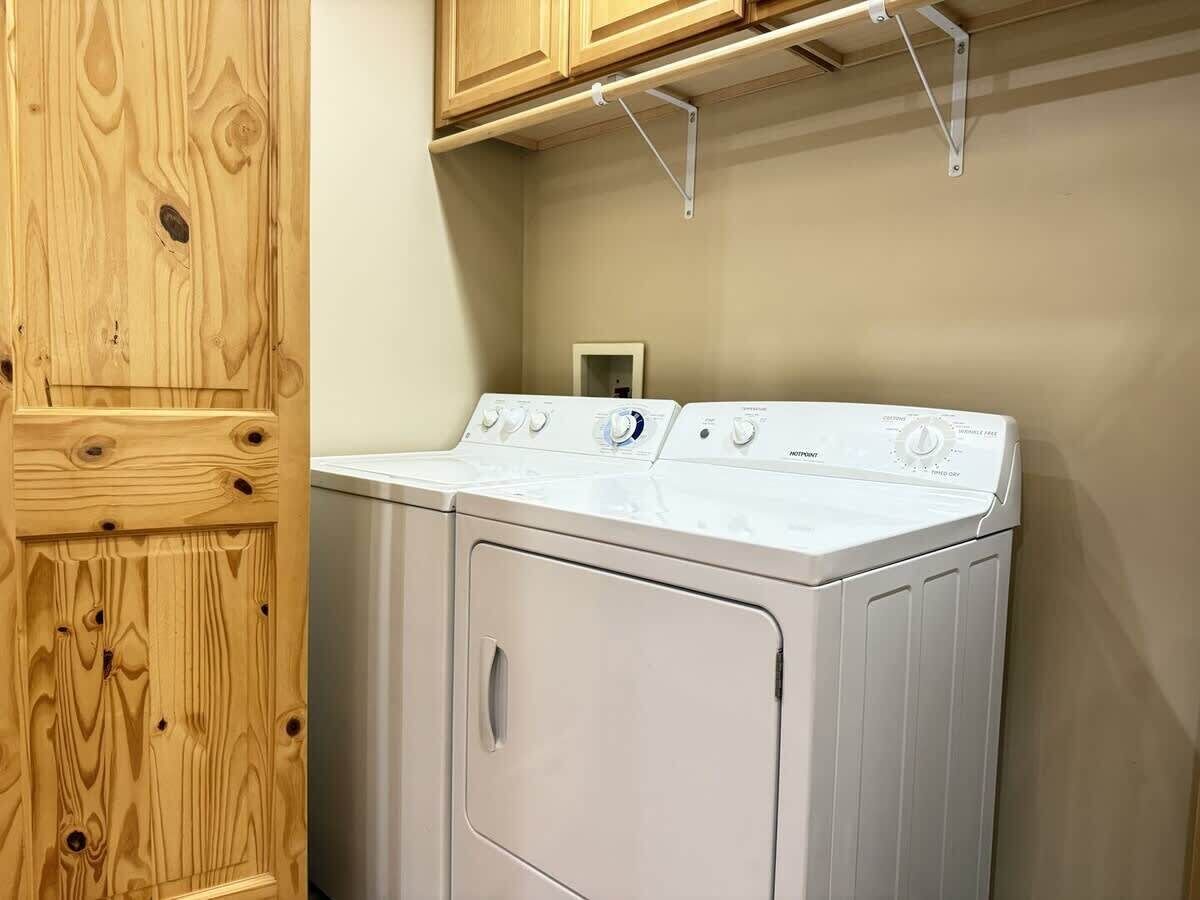 A laundry room with a front-loading washer and dryer, wooden cabinets, and a metal shelf above the dryer.