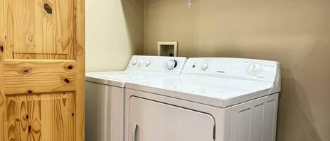A laundry room with a front-loading washer and dryer, wooden cabinets, and a metal shelf above the dryer.