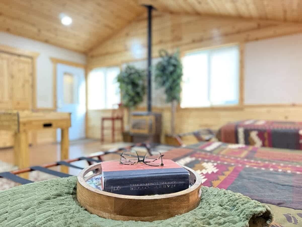 A cozy room with a wooden ceiling, a green knitted rug, a wooden side table, a bookshelf with books, and a colorful rug.