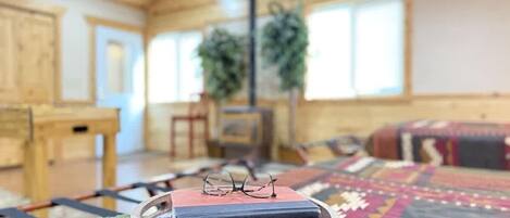 A cozy room with a wooden ceiling, a green knitted rug, a wooden side table, a bookshelf with books, and a colorful rug.