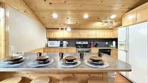 A modern kitchen with wooden cabinets, a central island with stools, and built-in appliances.