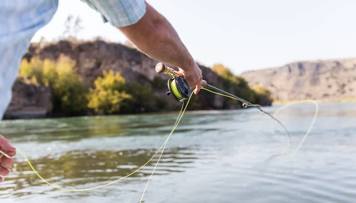 A person holding a fishing rod over water with a rocky landscape in the background.