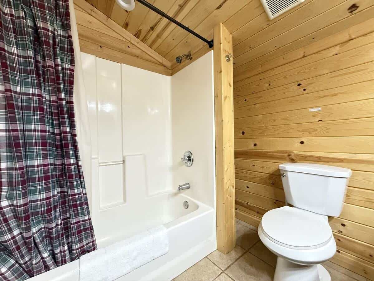A bathroom with a white bathtub, a white toilet, and a plaid curtain.