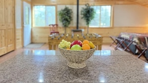 A room with a granite countertop, a woven fruit bowl, wooden cabinets, a fireplace, and a large window.