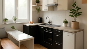 A modern kitchen with black cabinets, a white countertop, a sink, and a stove. There are potted plants on the windowsill and countertop. - Arena Suites Hannover (Hannover)