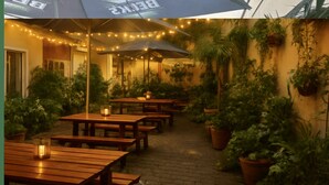An outdoor patio with wooden tables and benches, string lights, and potted plants. - Arena Suites Hannover (Hannover)