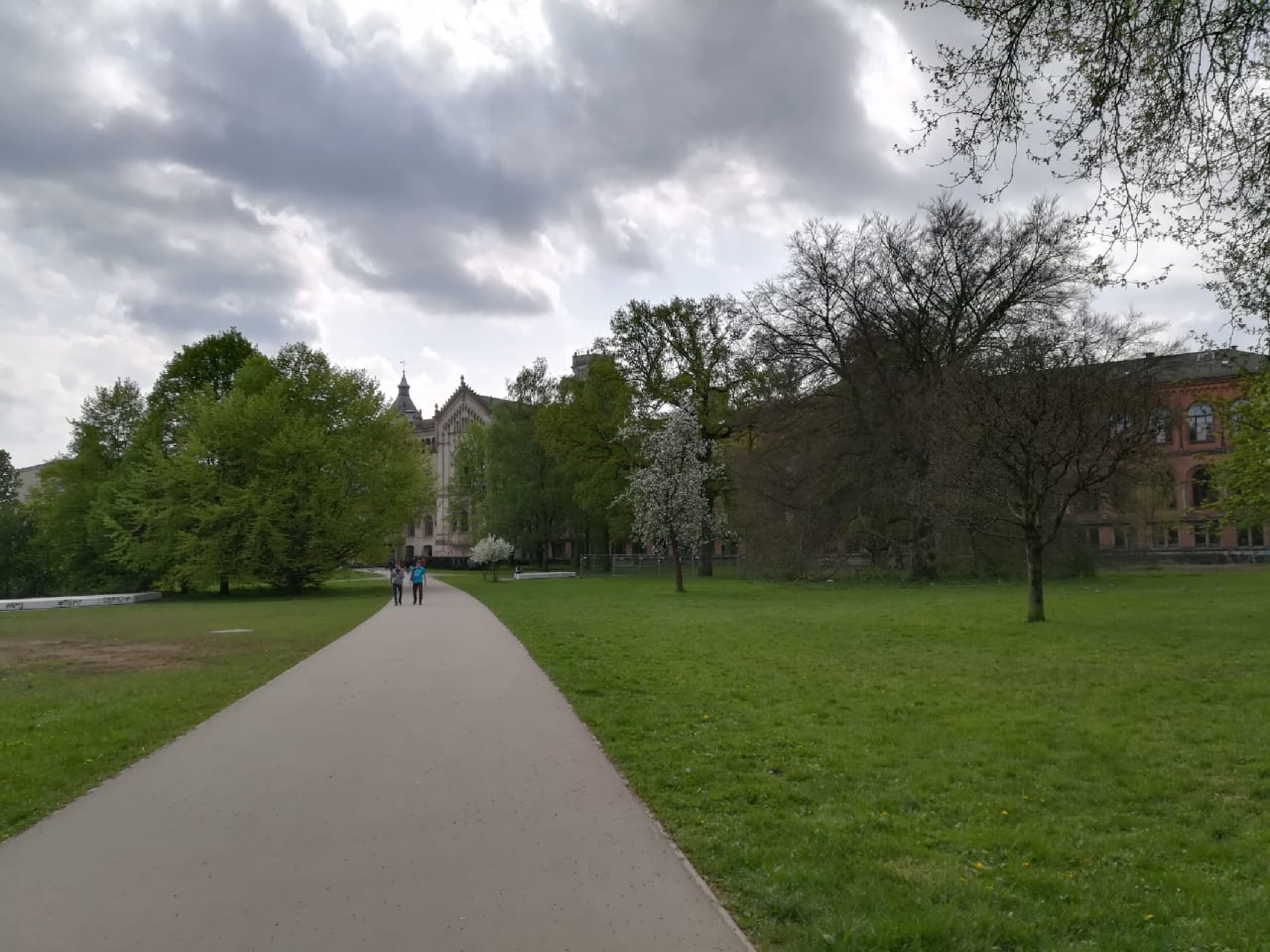 A pathway leading to a building with a traditional architectural style, surrounded by green grass and trees.