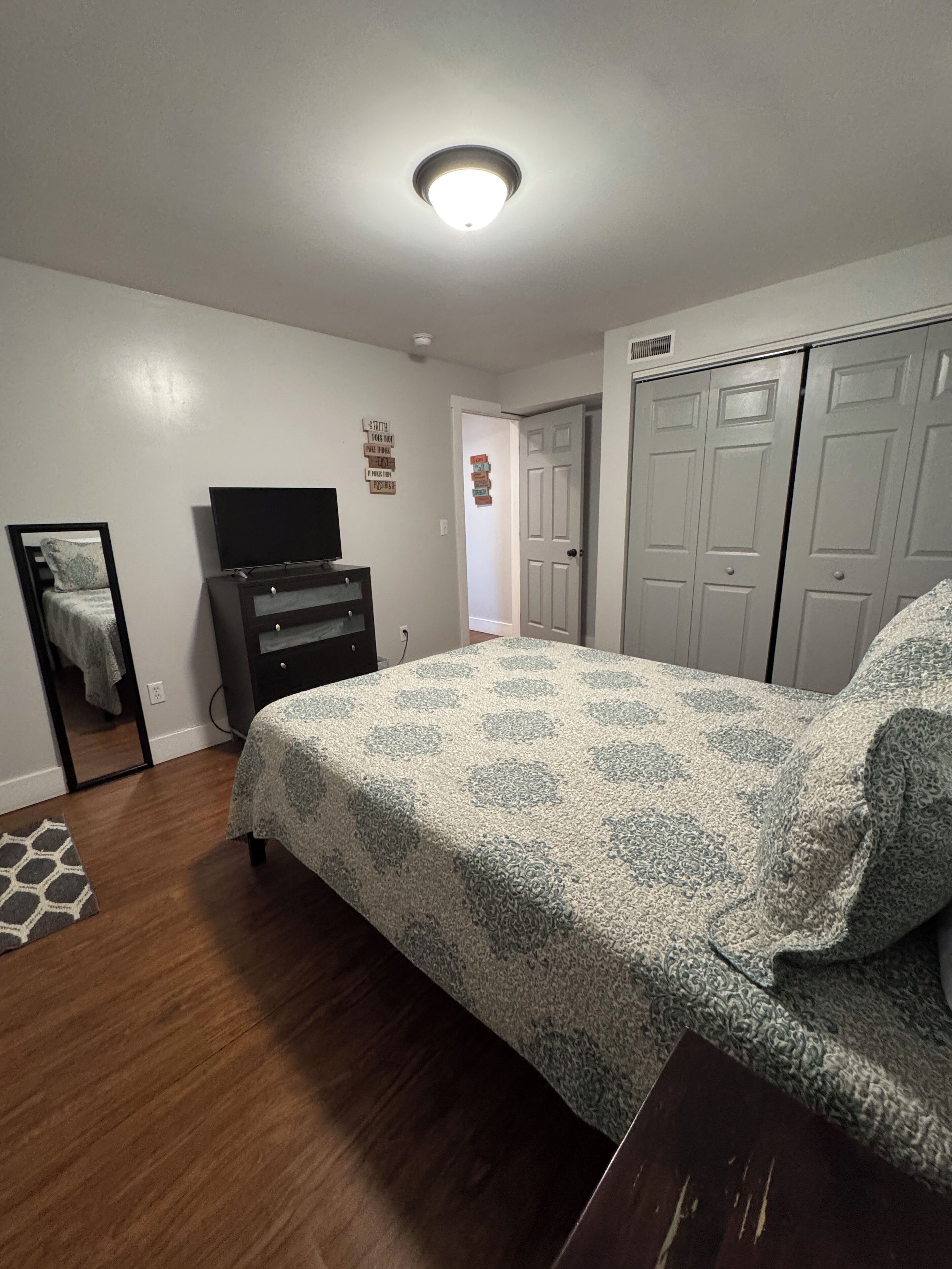A bedroom with a bed, dresser, TV, wardrobe, and a mirror.