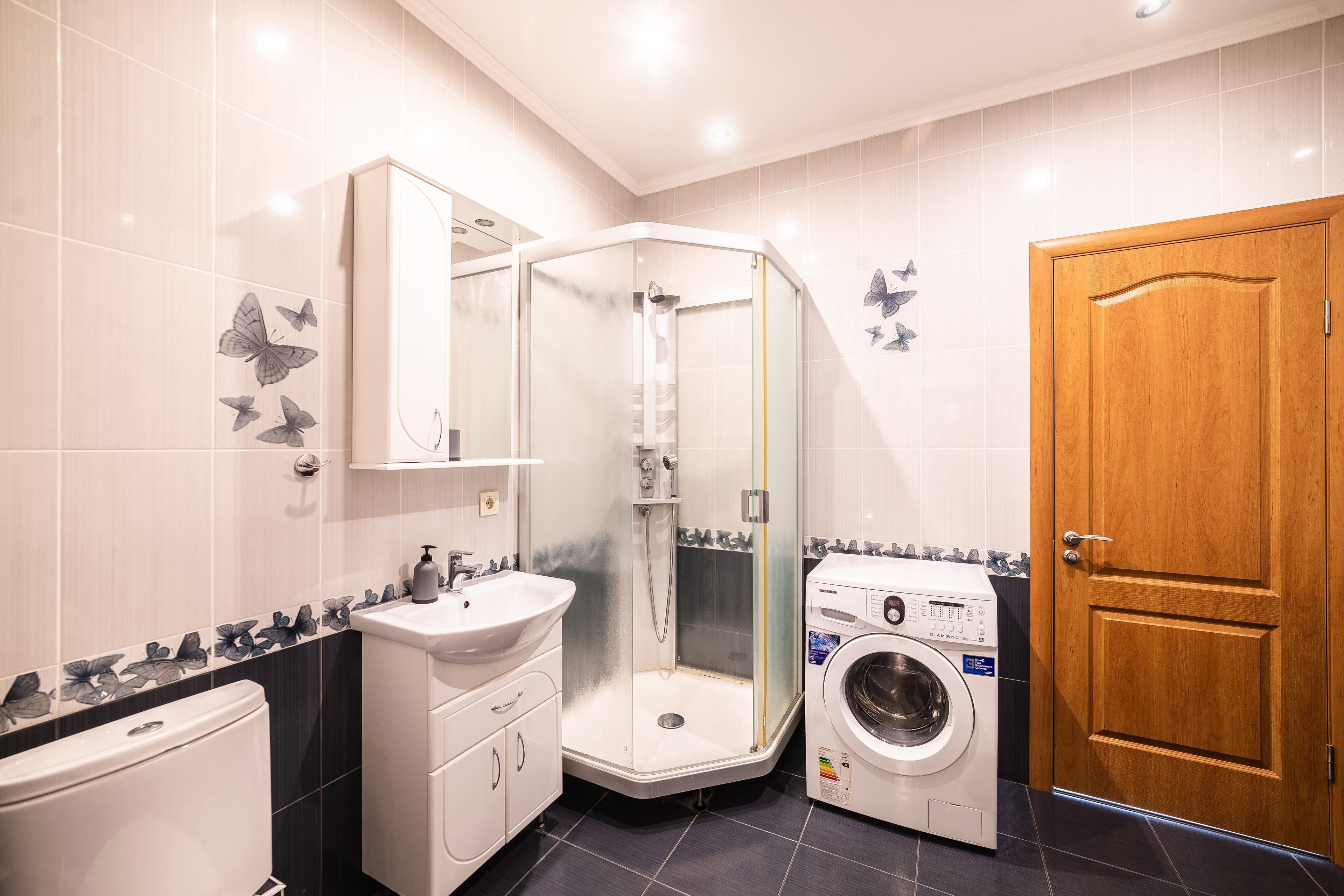 Een badkamer met een douche in hoekopstelling, een wastafel, toilet en wasmachine.