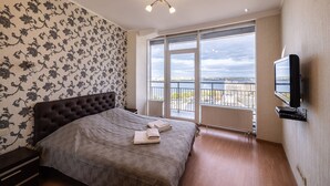 A bedroom with a large bed, a TV mounted on the wall, and a balcony with a view of the water. - Most City Apartments (Dnipro)