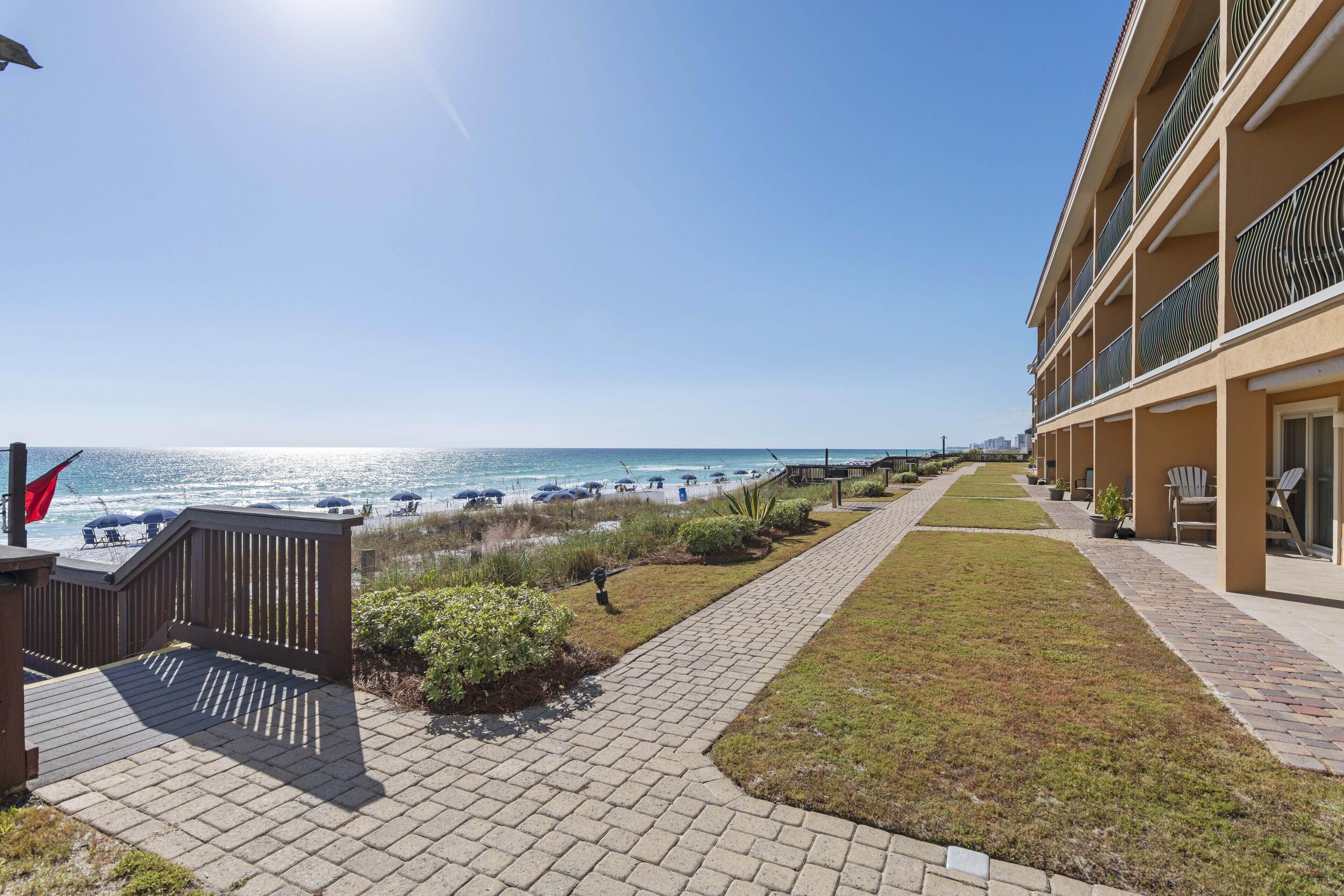 A hotel with a beachfront view, a paved walkway, and outdoor seating areas.
