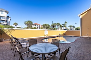 A poolside area with a round table and chairs, a swimming pool, and a building with balconies in the background. - 39- Recharge your happiness in this beautiful BEACH FRONT Condo! (Destin)