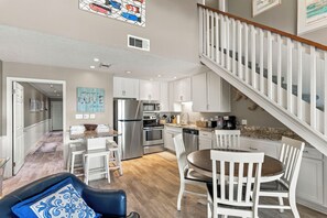 A modern kitchen with white cabinetry, stainless steel appliances, and a dining area with white chairs and a table. - 39- Recharge your happiness in this beautiful BEACH FRONT Condo! (Destin)
