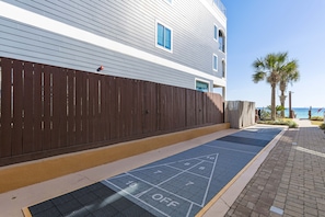 A wooden fence, a blue shuffleboard court, and a building with windows and a balcony. - 39- Recharge your happiness in this beautiful BEACH FRONT Condo! (Destin)