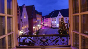 Uitzicht vanuit een raam op een straat met gebouwen, een kerstboom en een balkonhek.