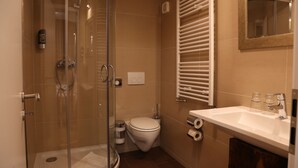 Een moderne badkamer met een douchecabine van glas, een wit toilet, een wastafel met spiegel en een handdoekrek.