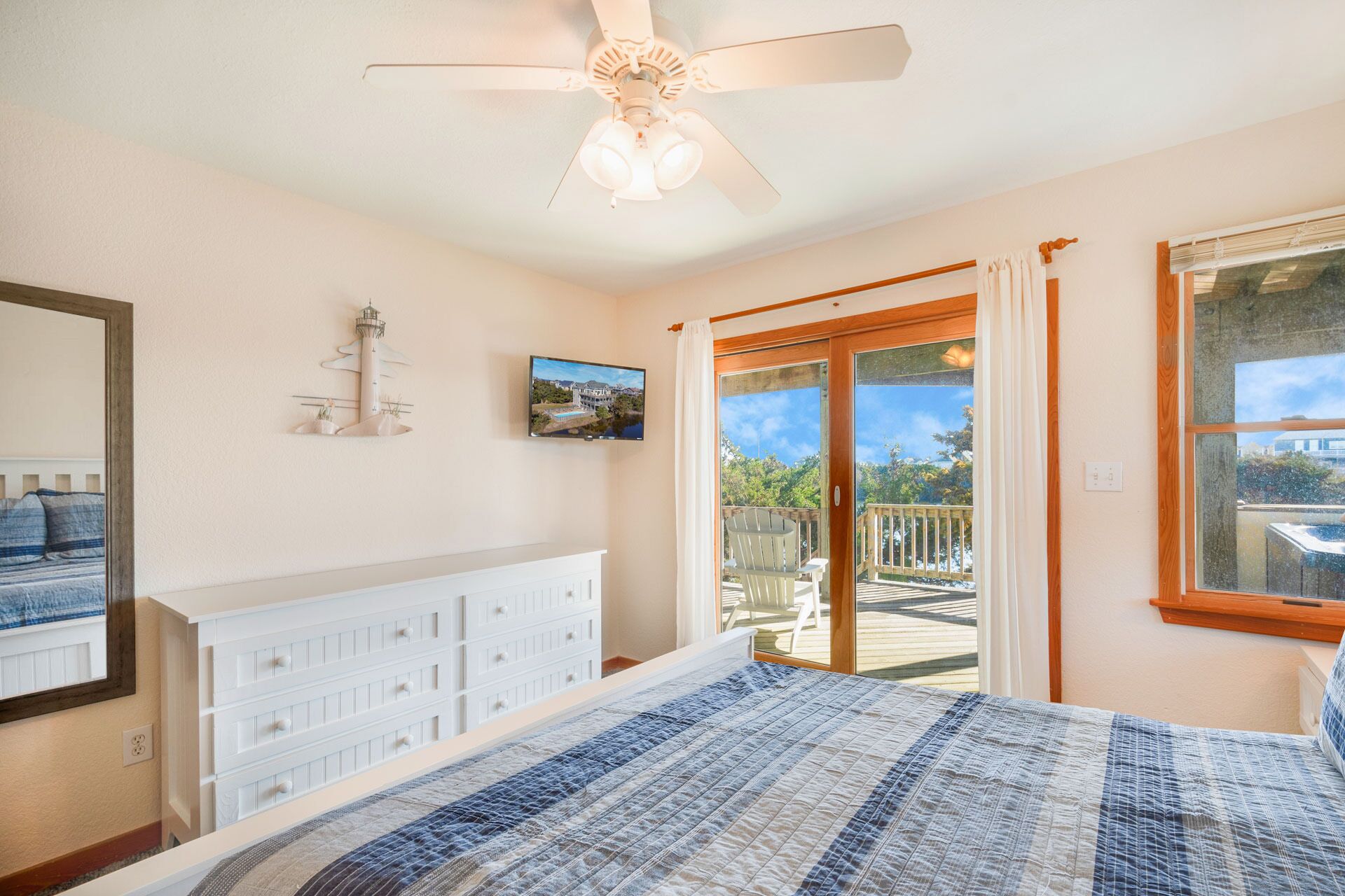 A bedroom with a bed, a ceiling fan, a dresser, a TV, and a balcony with a view of the outdoors.