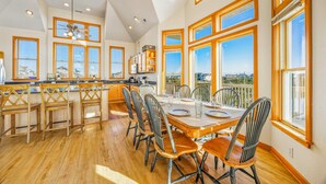 A spacious kitchen with large windows, wooden cabinets, and a dining area with a table set for six. - Oceanview Dog Friendly Home w/ Private Pool, Hot Tub, Game Room, Community Perks (Waves)