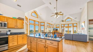 A spacious kitchen with wooden cabinets, a central island, and a dining area with a gray sofa. - Oceanview Dog Friendly Home w/ Private Pool, Hot Tub, Game Room, Community Perks (Waves)