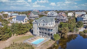 A large, multi-story house with a swimming pool, surrounded by trees and a body of water. - Oceanview Dog Friendly Home w/ Private Pool, Hot Tub, Game Room, Community Perks (Waves)