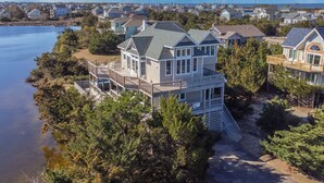 A multi-story house with a deck, surrounded by trees and a body of water. - Oceanview Dog Friendly Home w/ Private Pool, Hot Tub, Game Room, Community Perks (Waves)