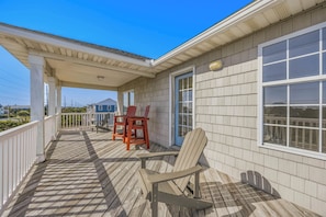 A covered porch with a wooden deck, two Adirondack chairs, and a table.