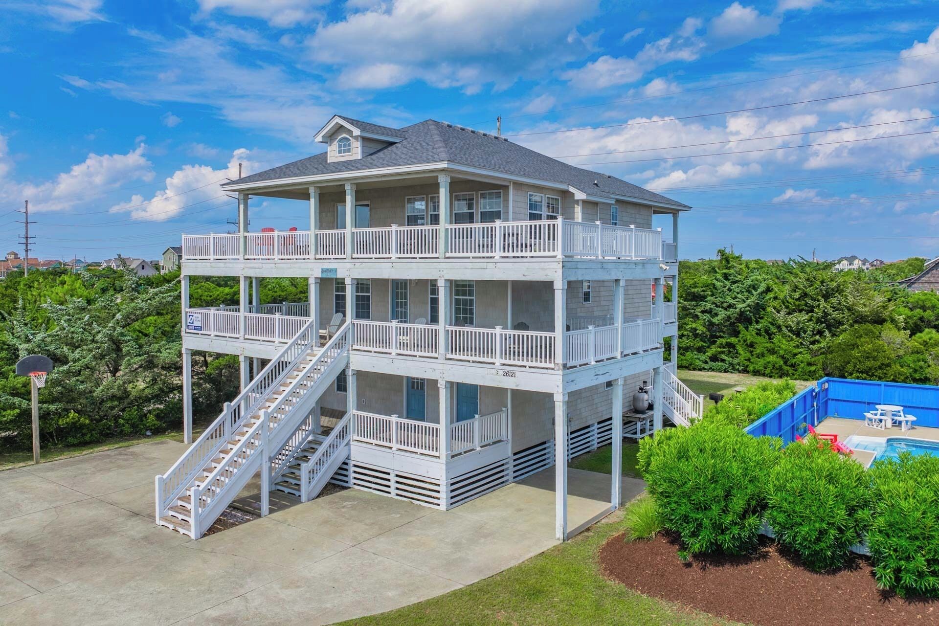 A multi-level building with a balcony on each floor, a staircase on the left, and a pool area to the right.