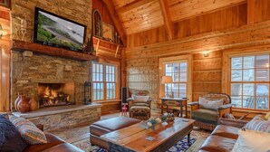 A cozy log cabin interior with a stone fireplace, leather sofas, and a large window offering a view of the outdoors. - Luxury Lodge on Private Mountain Top (Banner Elk)