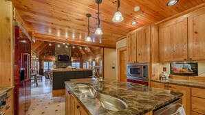 A spacious kitchen with wooden cabinets, a granite countertop, a large island with a sink, and a built-in oven. - Luxury Lodge on Private Mountain Top (Banner Elk)